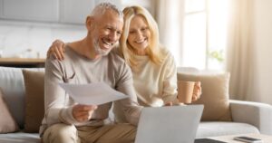 The Retirement Rule Millions Rely On Is Getting a Major Update Happy couple of pensioners sitting using computer and holding papers at home interior, senior husband and wife with laptop reading email and checking bills, doing paperwork with enthusiasm together