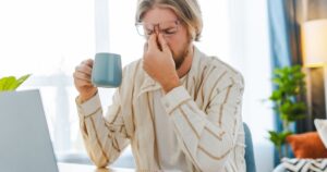 Stressed man in home office with headache while drinking coffee
