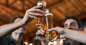 What Happens to Your Body When You Drink Beer Every Day: Expert Insight Cheers, friends and beer in restaurant with glasses as celebration for drinks, happiness or social bonding. Alcohol, men and people in pub for birthday party, event and reunion in Germany with toast