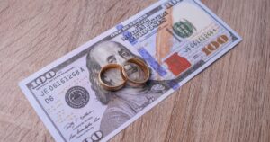 The 'Marital Loophole' That Zeroed Out This Couple's Taxes for 7 Years Wedding rings on money over wooden background. Price of getting married or divorce concept.