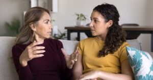 Happiness of mutual understanding. Loving mid aged mother talk to daughter teenager sitting on sofa at home speak to grown kid share life experience answer questions offer support give guidance advice