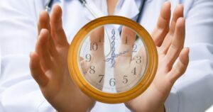 A person in a lab coat holds a clock with DNA strands at its center, symbolizing the research on genetic clocks that influence life expectancy and human lifespan.