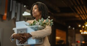 This Is the Real Reason Millions of Americans Have Left the Workforce Disappointed young african american businesswoman walking through the office, carrying a box of personal belongings after losing her job, reflecting on job loss and future uncertainty