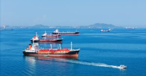 Trump Shelved Project Freedom: What You Need to Know LPG gas and oil tanker ships anchored in the ocean, with a fast patrol boat in the foreground. Global energy transport, war energy crisis, and Strait of Hormuz blockade concept