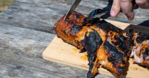 9 Foods Oncologists Wish You'd Eat Less Of a person carving charred, marinated pork tenderloin on a wooden board atop a rustic picnic table