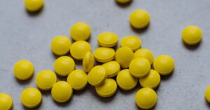 This Common Vitamin Could Be Dangerous If You Take Blood Thinners A collection of bright yellow pills scattered on a gray surface, ideal for health and wellness themes.