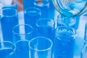 Why Leaving a Glass of Salt and Vinegar at Home Actually Makes Sense Close-up of blue liquid being poured into glass test tubes in a laboratory setting.