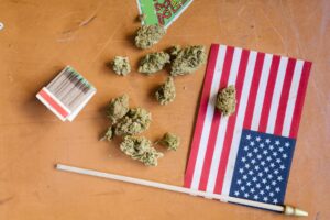 New Poll: Most Americans Now Support Legalizing Marijuana Nationwide Top view of cannabis buds, matchsticks, and American flag on a wooden table.