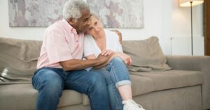 7 Behaviors Men Show When They Struggle With Emotional Intimacy Senior couple embracing warmly on a sofa at home, showcasing love and togetherness.