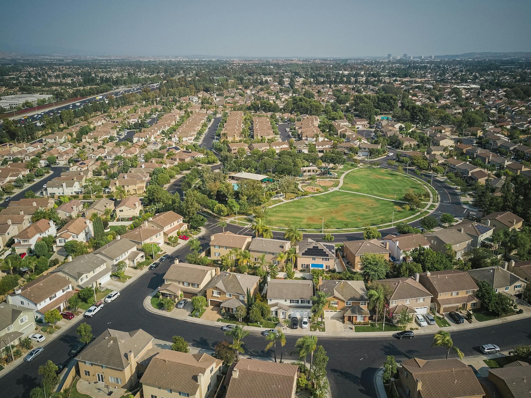 Drone shot of a spacious suburban neighborhood featuring a central park with numerous houses.