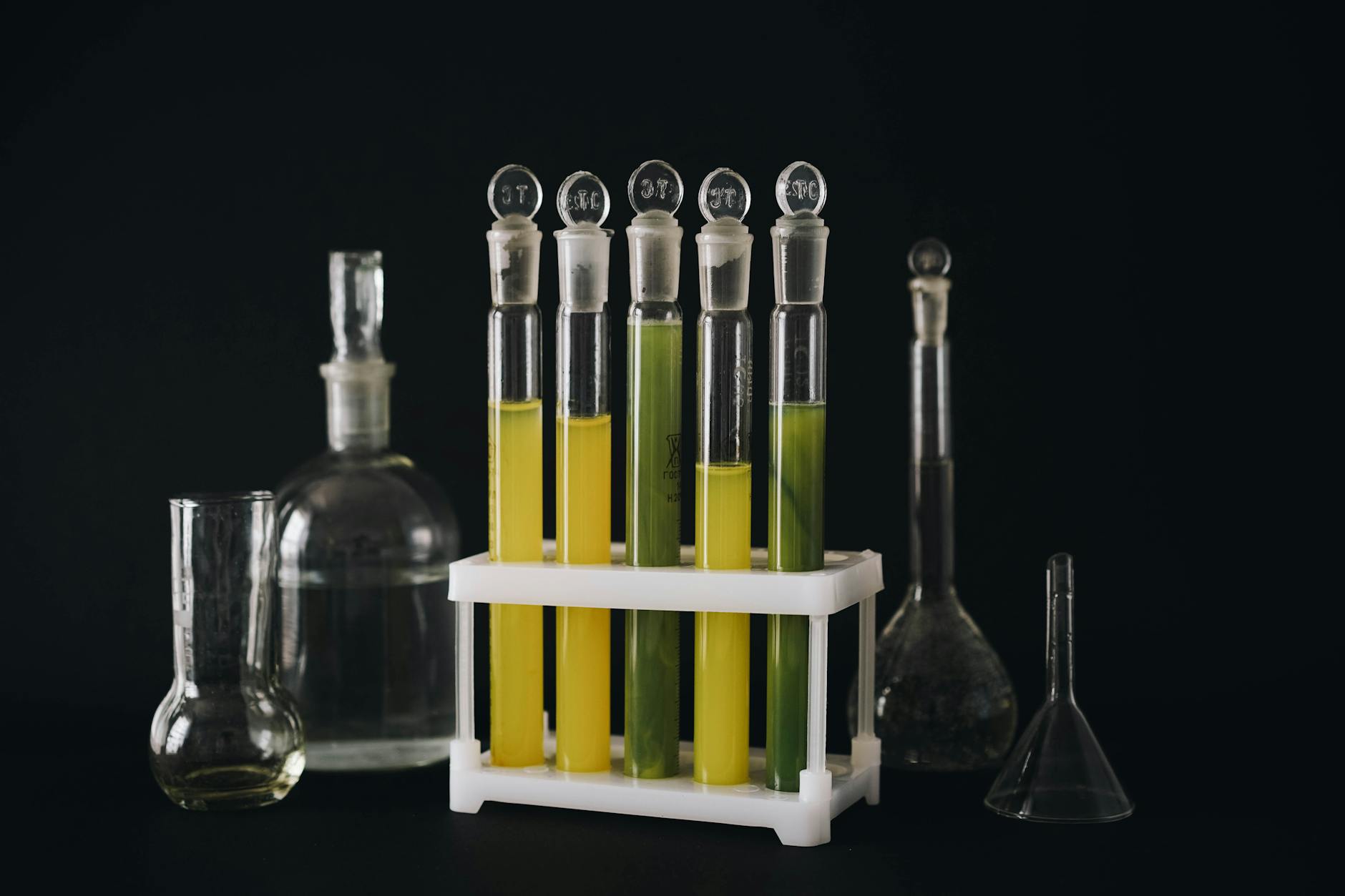 A collection of vibrant liquids in test tubes against a black background, showcasing chemistry equipment.