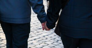 10 Old-Fashioned Date Ideas Smart, Happy Couples Are Bringing Back Back view of a couple holding hands walking on a cobblestone street.