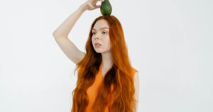 Portrait of a red-haired woman playfully balancing an avocado on her head.
