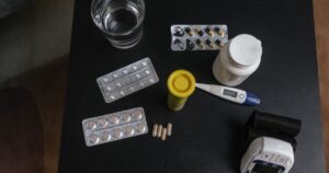 7 Common Medications You Shouldn't Take With Your Morning Coffee Top view of various medications, tablets, and medical devices on a table with a glass of water.