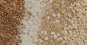 9 Whole Grains That Can Help Improve Your Cholesterol Levels A variety of grains and cereals including oats, rice, and buckwheat arranged in a flat lay.