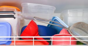 Common Kitchen Item That Oncologists Are Begging People to Throw Out Dish drying rack above sink closeup. Plastic containers and lids drying. Kitchen organizer detail. Clean tableware after washing. Home dishwashing routine. Household cleaning process.