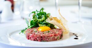 Beef tartare with arugula salad, egg yolk and crisp bread chips on white plate