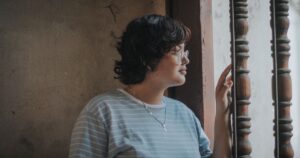 A thoughtful woman with short hair and eyeglasses gazes out a window.