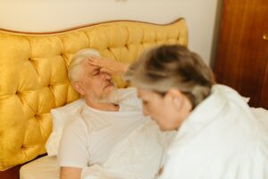 An Alzheimer's Patient Recovered Speech and Memory After One Dose of This Experimental Drug An elderly man in bed being checked for fever by a caregiver, suggesting illness or resting state.