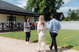 Mortgage Rates Hit 6.52% — Should You Buy Now or Keep Waiting? A diverse group viewing a house for sale with a real estate agent outdoors.
