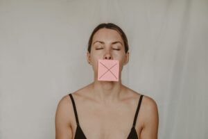 A Diagnosed Psychopath Explains Why His Manipulation Tactics Were So Hard to See Young slender woman with closed eyes and mouth covered with sticky note showing cross on white background