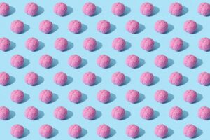 How ADHD May Influence Creative Thinking, According To New Research Creative composition of pink brain models in a repeating pattern on a light blue surface, showcasing abstract thinking.