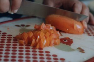 Hands chopping a tomato on a decorative cutting board in a kitchen setting.