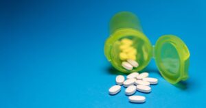 7 Aleve Long-Term Side Effects Most People Don't Know About Image of a green pill bottle with white tablets scattered on a blue background, symbolizing healthcare and medication.