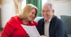 Elderly couple joyfully reading a paper together on the couch in a cozy indoor setting.