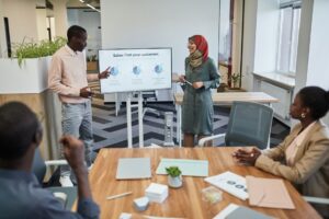 The Job AI Was Supposed To Kill Needs More Humans Than Ever A diverse team engaging in a business meeting focused on sales strategy with visual aids.