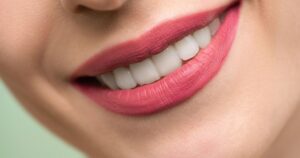 New Medicine May Help Humans Grow a Third Set of Teeth Vivid close-up image of a woman's smile showcasing red lipstick and white teeth on a light background.