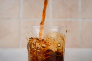 A Heart Surgeon Calls This Everyday Drink "Liquid Death" — Here's Why A close-up capture of soda being poured into a glass, creating a splash effect.