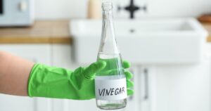 The $3 Trick That Actually Gets Rid of Musty Closet Smell Overnight Person wearing rubber glove holding a glass bottle of vinegar