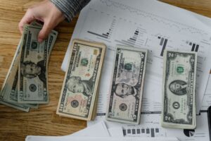 Person holds US dollars over financial papers, showing income or budget analysis.