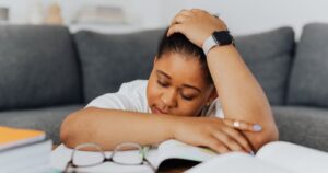 A woman rests on textbooks, exhausted from studying in her cozy living room environment.