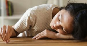 She Started With Weed at 12. By 30, She Was Spending $450 a Day on Heroin. Woman lying on wooden table, appearing emotional, with a small object in hand.