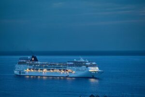 The Mile-Long Freedom Ship 'Floating City' Could Actually Happen A cruise ship glides through calm waters at dusk, illuminated against the serene evening sky.
