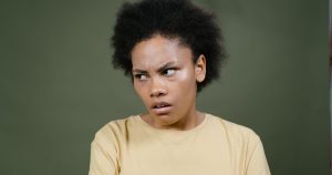 10 Phrases People Who Are Mentally & Emotionally Messed up Usually Say in Casual Conversation Close-up of a young woman with afro expressing a pensive mood against a green background.