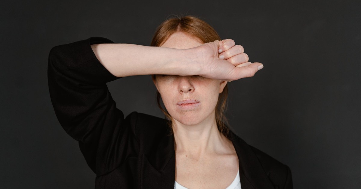 Close-up of a woman in a black blazer covering her eyes with her arm.