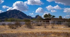 10+ Quaint Arizona Towns Where You Can Retire on $2,800 a Month (Or Less) Charming rural farmhouse set against Arizona's stunning mountain scenery, under a bright blue sky.