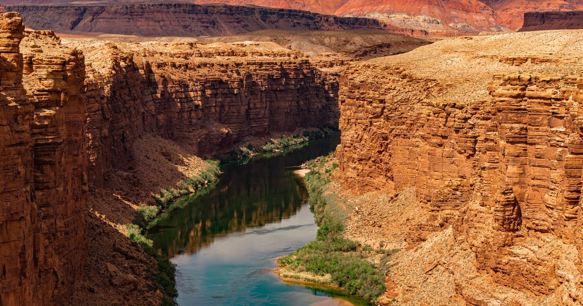 Stunning view of the Grand Canyon's rugged sandstone cliffs and serene river bend under a warm sunset.