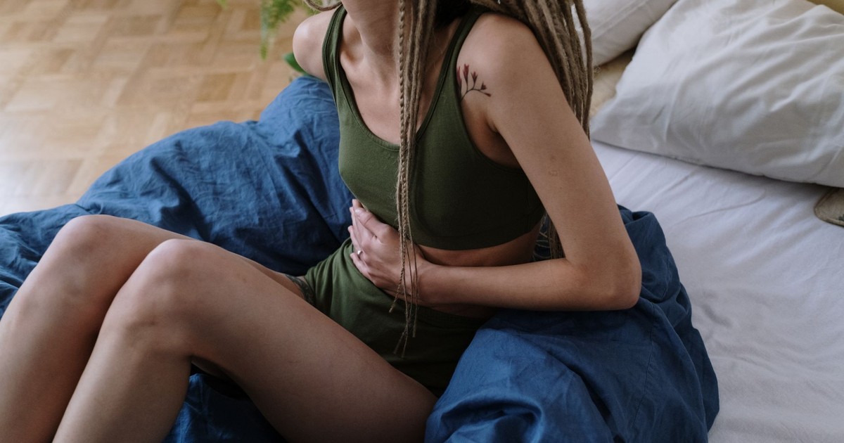 Woman sitting in bed holding her stomach, indicating pain or discomfort, possibly due to cramps.