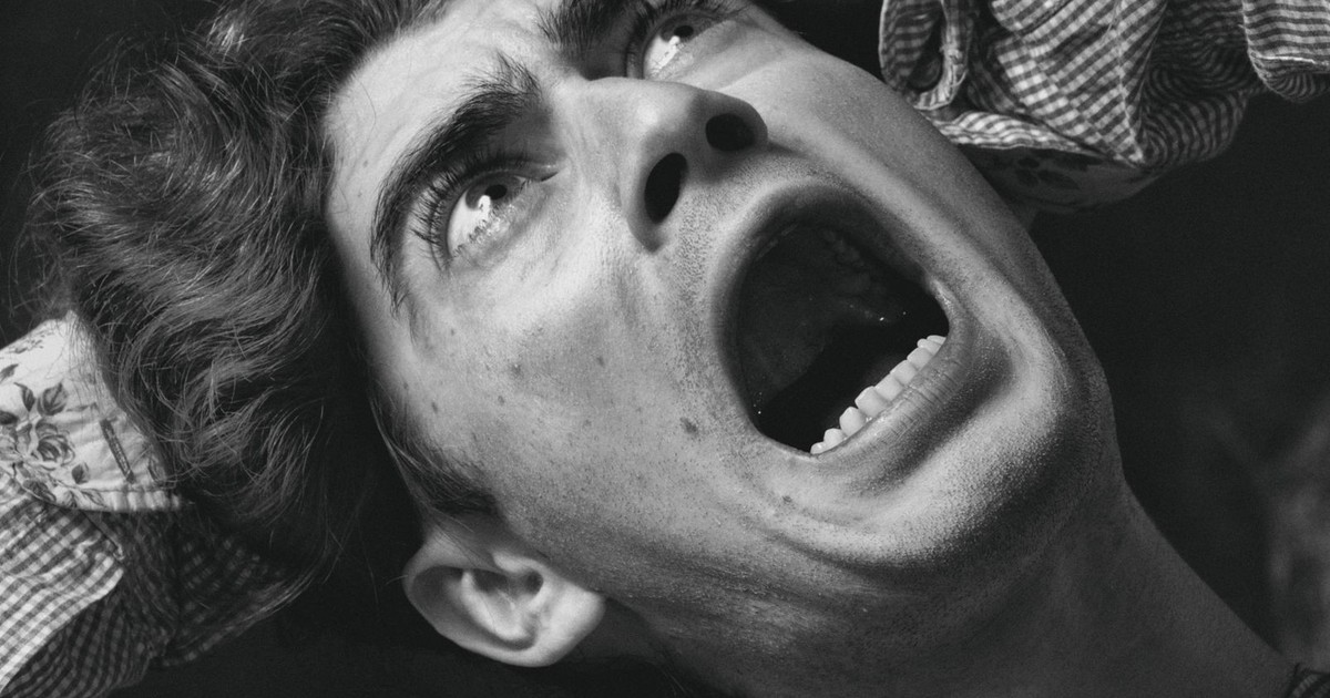 A dramatic black and white close-up of a man with an open mouth showing fear.