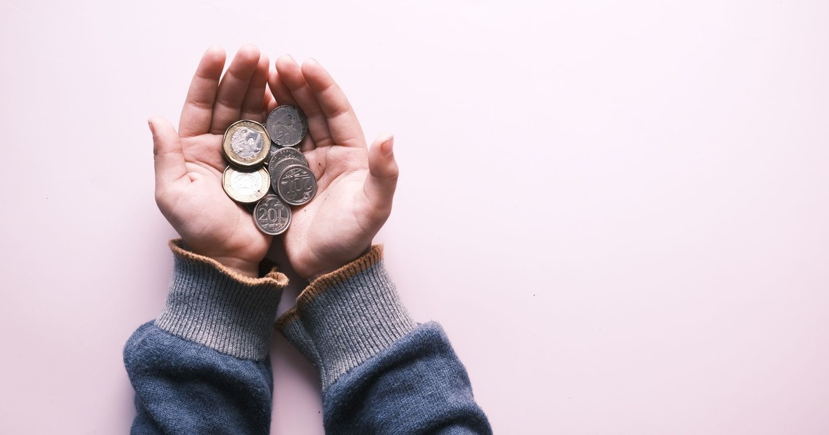 Close-up of hands in sweater holding various coins, indicating savings and finance on a white background.