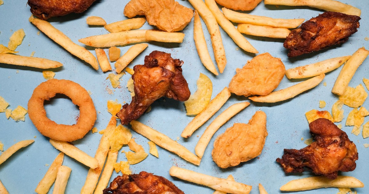 From above of french fries and grilled chicken wings with golden deep fried onion rings and nuggets with chips on blue background in bright studio