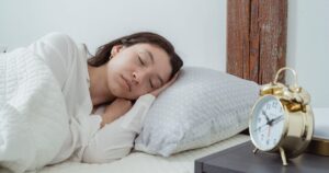 13 Tips to Help You Fall Asleep Fast Young calm female with dark hair lying on side with hand under head on white comfortable bed under blanket while sleeping in morning time