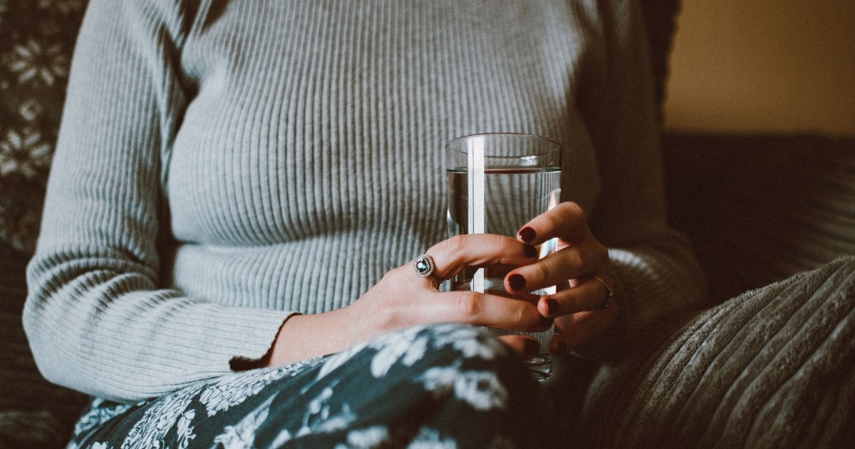 Close-up of a woman holding a glass of water while sitting indoors, conveying calm and relaxation.