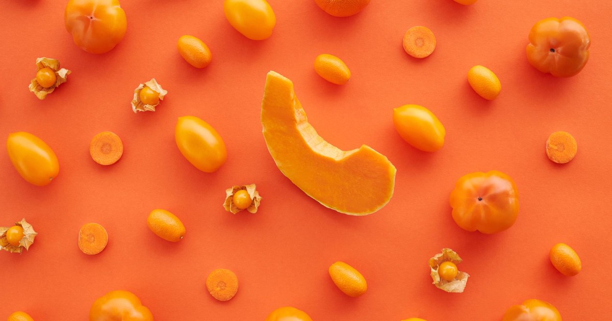 Top view of assorted orange fruits and vegetables on orange surface, offering organic health benefits.
