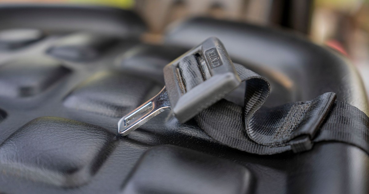Detailed macro shot of a metal seatbelt buckle on a textured black vehicle seat.