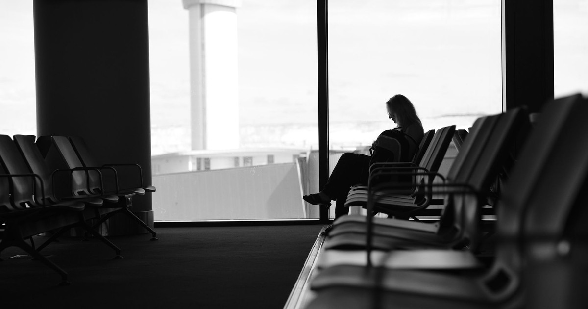 Silhouette of a woman sitting in an airport terminal lounge, with view of control tower.